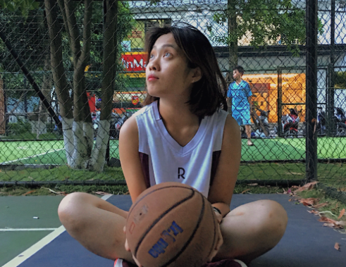 woman sits on a basketball court holding a basketball