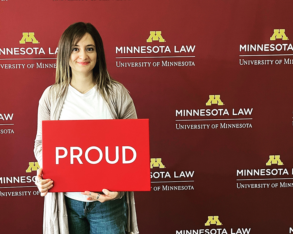 Shaghek Manjikian holding a "proud" sign in front of a Minnesota Law photo backdrop