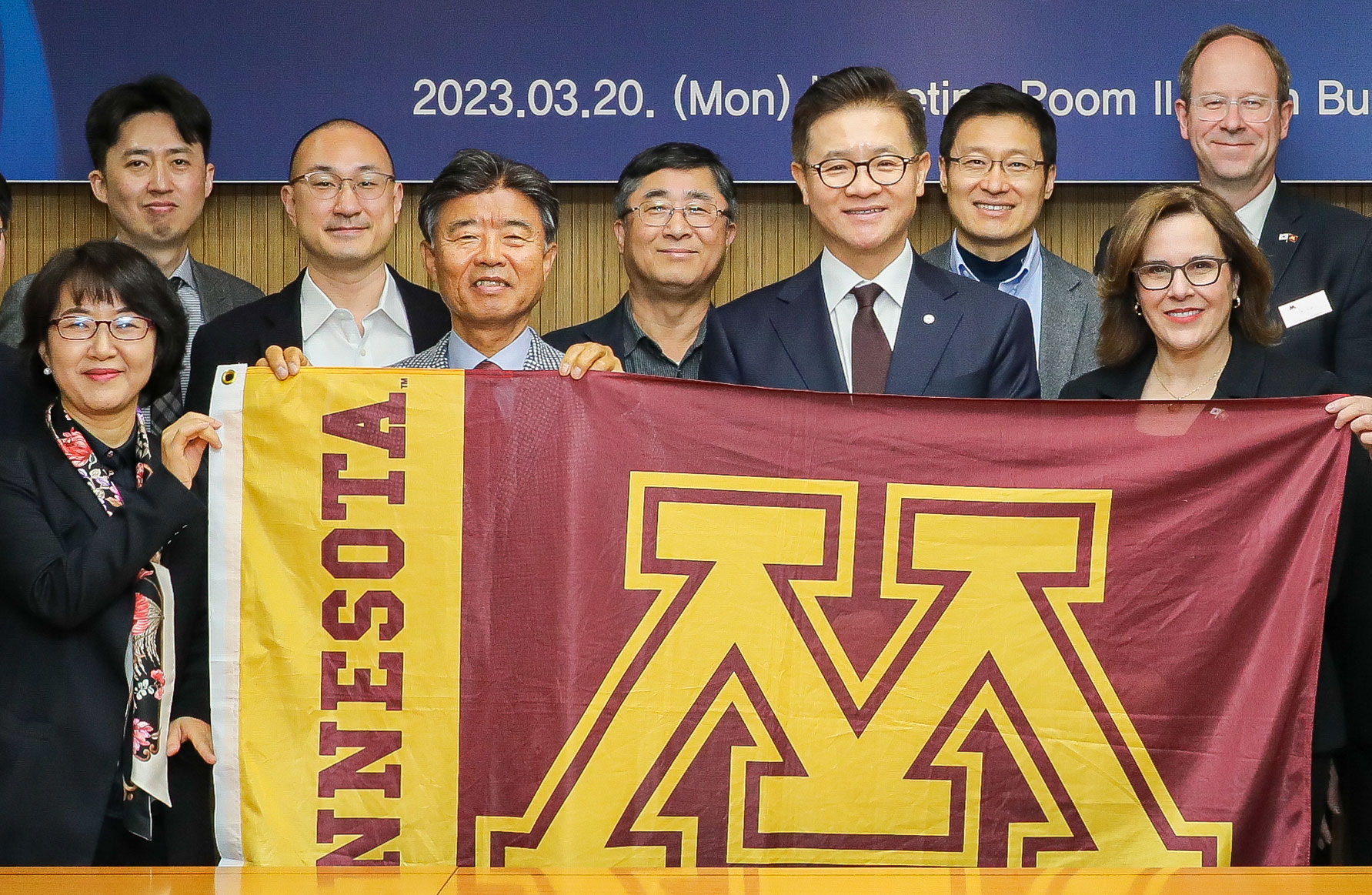 President Gabel posing with Korean colleagues behind a flag with the University of Minnesota logo