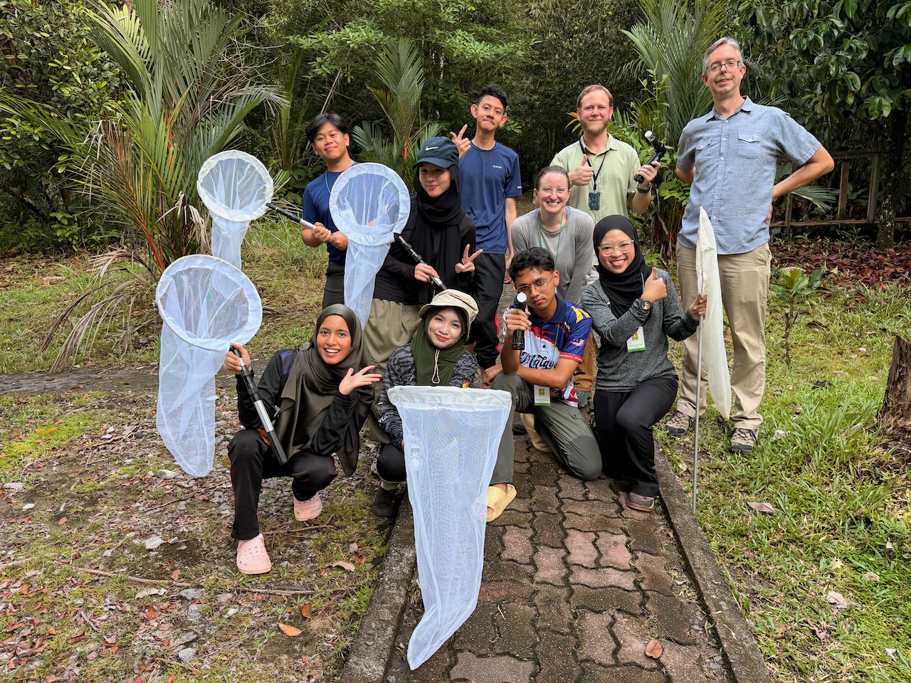 A group of people stand on a path in the forest with mosquito nets