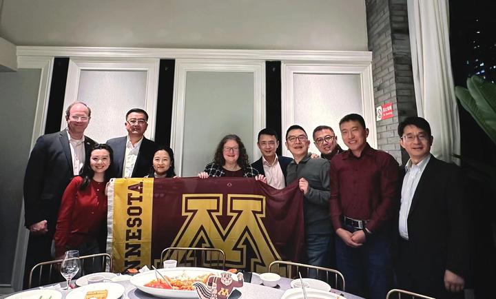 Provost and dinner guests posing with a UMN flag