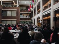 a wide photo of the audience sitting at round tables in a large atrium